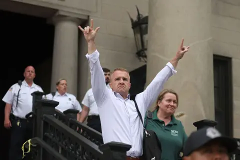 Karen Read found not guilty of murdering police officer boyfriend Getty Images Aidan "Turtleboy" Kearney, wearing a white shirt gestures outside the courthouse. His hand gesture means "I love you" in American Sign Language