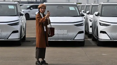 How China made electric vehicles mainstream Getty Images A woman takes a selfie in front X9 electric vehicles by Chinese EV manufacturer XPeng, are loaded on ship of the NYK line during a ceremony in the Port of Guangzhou, China's southern Guangdong province, on 22 February, 2025.
