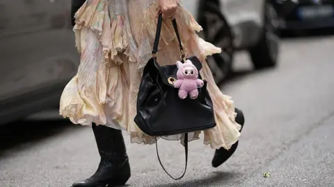How the Pop Mart dolls conquered the world Getty Images A pink Labubu doll clipped to a black handbag, carred by a woman