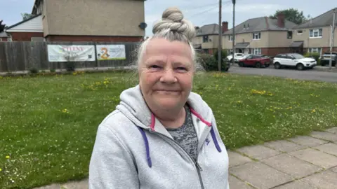 Big Venture Centre stepping in where 'everyone is struggling' Tracey Walters smiling for the camera. There is a grassy area behind her with daffodils. She is wearing a nike jacket and a grey t-shirt underneath. She is wearing her hair as a bun on top of her head.