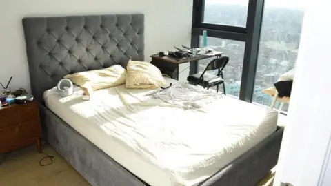 PhD student Zhenhao Zou, who raped 10 women, jailed for 24 years Met Police The bedroom of the house where Zhenhao Zou lived. There is a grey bed with a white sheet over the mattress. To the right of the bed is a desk and chair and to the right the window overlooks London