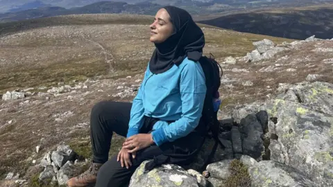 Gary Oldman and Strictly hosts Tess and Claudia join David Beckham Zahrah Mahmood/PA Wire Zahrah Mahmood, a woman in a blue top, black trousers, brown walking boots and black hijab, sits with her eyes shut on a rock surrounded by countryside