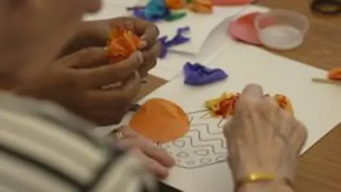 Covid inquiry begins examination of impact on social care sector Close-up of two pairs of hands working on a collage - one pair is that of an old person, the other of a younger care worker. This shot was taken in June 2025.