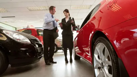 What's behind the mis-selling complaints? Getty Images Man and a woman in smart clothing talk in a car dealership, standing between new cars