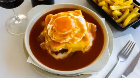 Japanese fruit sando hits high streets JackF/Getty Images A Francesinha - a sandwich with a fried egg on top that is swimming in a gravy-like sauce - is served on a white plate on a white table, next to a tray of chips