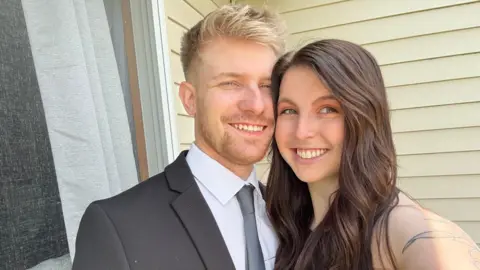 'It doesn't matter that my boyfriend is 5ft 6in"' BBC Ashley, a young woman with long brown hair wearing a sleeveless top, takes a selfie with Joe, a young man with blonde hair wearing a grey suit jacket, white shirt and grey tie.