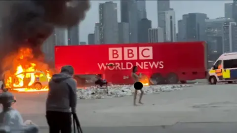 British man charged over mock Disneyland wedding to child had been investigated by BBC Twitter A still from a video which shows Jhaj, naked but sensored, standing infront of a big red lorry that has the BBC World News logo on it, and part of the lorry is on fire. A videographer can be seen in the foreground.