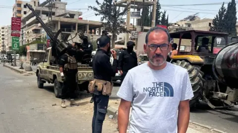 BBC team detained by Israeli forces in southern Syria BBC Feras Kilani stands on a street in Damascus, Syria. In the background, Syrian security forces are deployed with a truck-mounted anti-aircraft gun (7 May 2025)