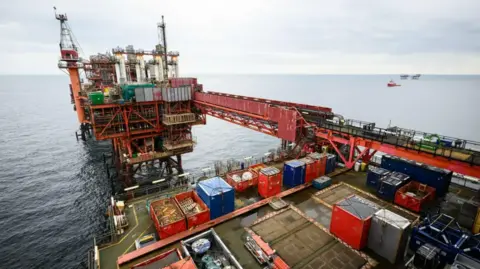 Kemi Badenoch calls for end to windfall tax on oil and gas companies PA Media A general view of an oil rig. The structure is mainly red with a number of multi-coloured shipping crates on the deck.