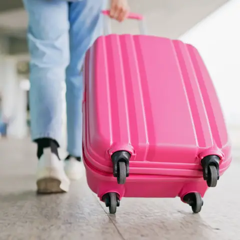 How budget airline baggage confusion triggered EU legal row Getty Images A young woman wearing light jeans and white trainers pulling a bright pink suitcase in an airport