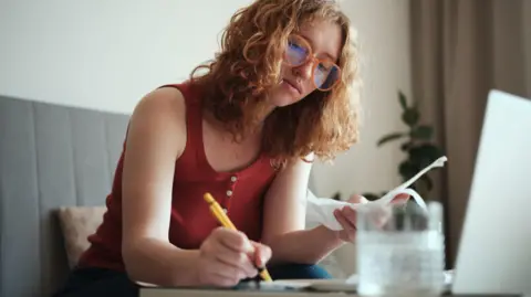 Bank of England expected to hold interest rates Getty Images Woman wearing glasses sits at a table with a pen in one hand and receipts in the other.