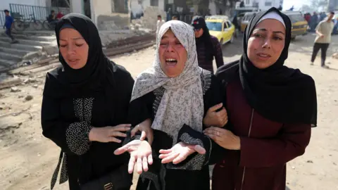 At least 81 people killed in Israeli strikes in Gaza, Hamas-run health ministry says Reuters Three women linking arms with expressions of despair, with woman in the centre crying. Woman on left of image is wearing a black abaya with a black hijab, woman in centre, the same with a white printed hijab and the woman on the right is wearing a burgundy abaya with a black hijab and white bandana underneath it.