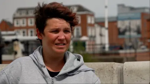 Ship on fire at Hull's Albert Dock as roads and shops are closed Becki Bowden/BBC A woman with short brown hair and wearing a grey hoodie stands next to Hull Marina. There are several large buildings behind her.