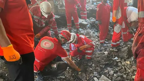 Trump's order to leave Tehran adds to fear as Iranians share 'last photo of home' EPA A handout photo made available by Iranian Red Crescent Society (IRCS) shows rescuers working at the site of an airstrike on a residential area in Tehran. Many men wearing red uniforms dig through rubble.