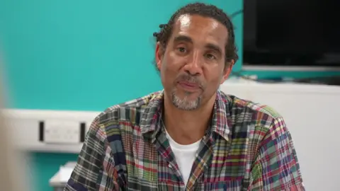 'Child Q case made me fear could this happen to me' Paul Anderson sits at the table taking part in the discussion, a bright blue wall behind him. He has his hair tied back and wears a colourful plaid shirt