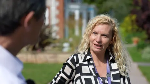 Hospice staff tell BBC what they think about bill Vicky Bartlett, who has long blonde wavy hair and is wearing a black and white patterned top and purple lanyard.