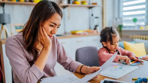 Council tax expected to rise by 5% a year Getty Images Young mum sits looking at bills, with her daughter sitting at the table next to her playing
