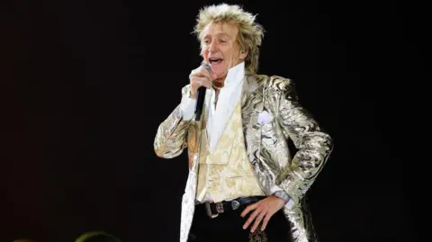 'I wish they wouldn't call it the tea time slot' Getty Images Rod Stewart talks into a microphone with one hand on his hip, while wearing a silver paisley coat and a brocaded waistcoat. He looks fabulous.