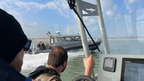 Smugglers deploy 'taxi boats' to collect migrants off the French coast Marianne Baisnée/BBC Two men sit in the patrol boat, with a second patrol boat on the water across from them