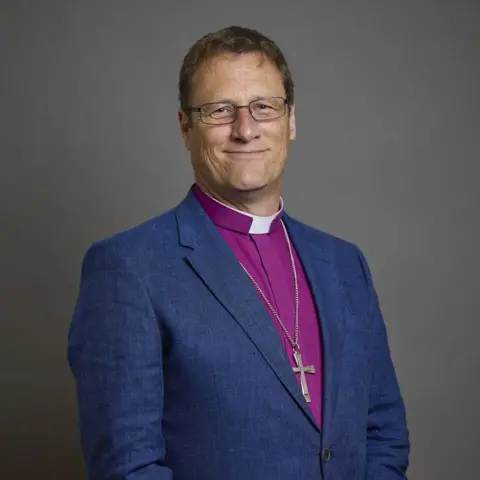 A preacher asked me out and then started stalking me House of Lords/Roger Harris A portrait of Bishop of Leicester, Martyn Snow, wearing a navy blue blazer with a pink shirt. He is smiling and wearing glasses, with a grey background.