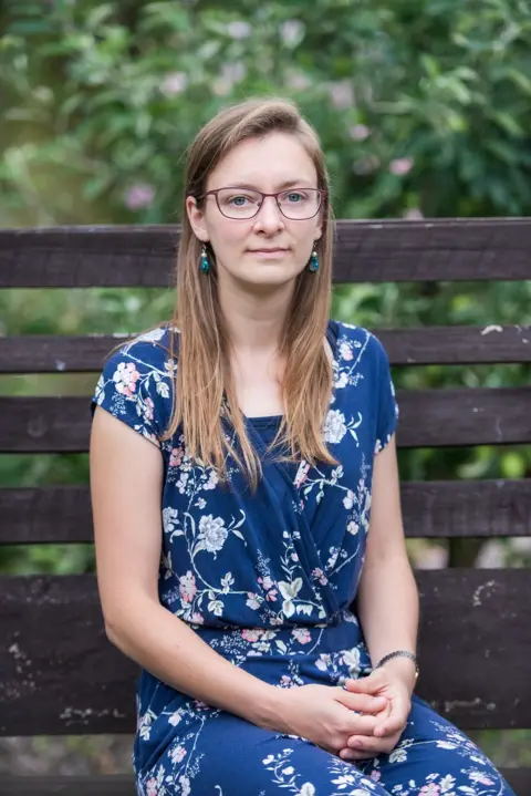 A preacher asked me out and then started stalking me A woman in a blue floral dress sits on a brown bench with a green and pink flowery bush in the background.
