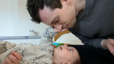 Paternity leave in UK is outdated and unequal, say MPs BBC A man leans down and closes his eyes as his smiling baby reaches out to touch his face