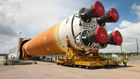 Trump-Musk row fuels 'biggest crisis ever' at Nasa NASA Nasa's SLS rocket lying horizontally and on supports and being wheeled into an enclosure. The rocket appears gigantic in compariosn to engineers sitting alongside the vehicle.