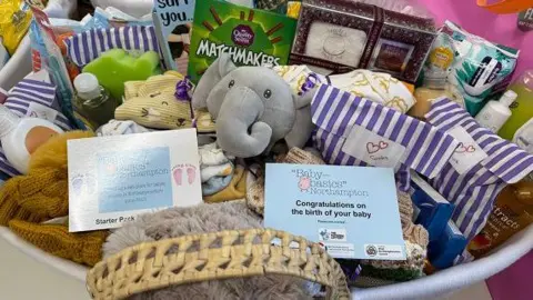 Wollaston charity supports one in 16 babies across the county Annabel Amos/BBC Basket containing some slips saying "congratulations on the birth of your baby". There are stuffed toys including an elephant, toiletries and chocolates.