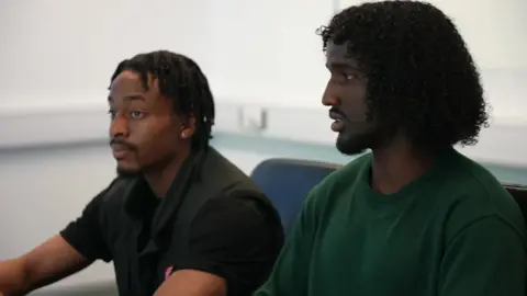 'Child Q case made me fear could this happen to me' Tosin, 20, and Adnan, 18, sit at the table in an office room taking part in the discussion. Tosin, wearing a black sleeveless jacket, looks straight ahead, listening, while Adnan, in a dark green top, is speaking.