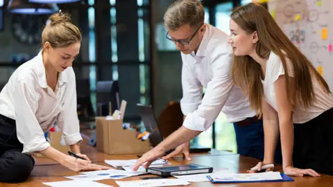 UK's data agency has 'deep seated' issues, review finds Getty Images Three people lean over a desk looking at a paper with data graphs on it, holding pens and in discussion.