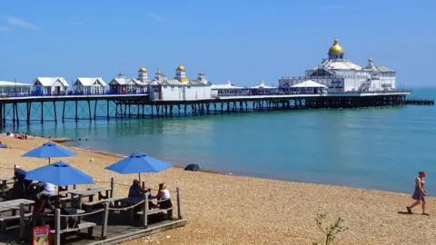 Amber thunderstorm warning in force after UK's hottest day BBC Weather Watchers/ Peter and Leah A man walking across golden sands bordering bright blue seas in Eastbourne
