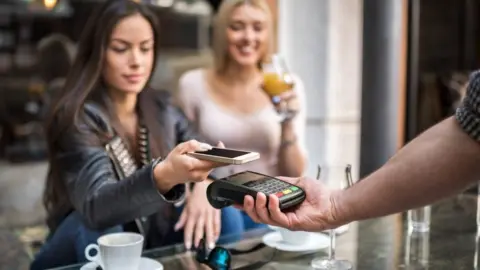 When will interest rates go down again and how do they affect mortgages? Getty Images A woman in a leather jacket paying for her drinks by tapping a card machine with her phone