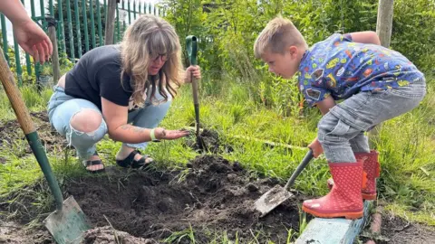 Ban 'no ball games' signs to get children off devices, play experts say Hayley Clarke/BBC Sam, who has brown hair is showing her son something small she found in the clay in her hand. Chester is wearing red wellies and digging with a shovel in the park.