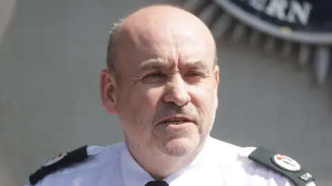 Police deploy more officers after 'mob violence' Pacemaker Press A close up of a police constable. He's wearing a white shirt with lapels on the shoulders.