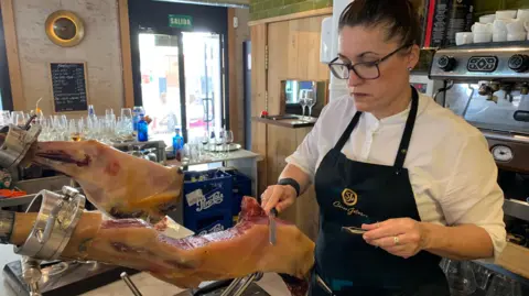 US tariff turmoil makes Spain's flagship foods seek other markets Guy Hedgecoe A leg of Spanish ham, or jamon, being carved at a bar in Seville