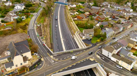 'The Heads of the Valleys road swallowed part of my garden' FCC Construction An aerial view of the Heads of the Valleys road and John Watkeys' house. A bridge with a road on it can be seen crossing above the dual carriageway below, with cones going down the middle of each carriageway. On the upper level, a row of terraced houses can be seen right right by the side of the road with a housing estate to the right hand side.
