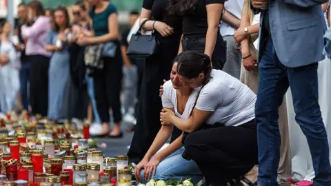 School killings leave stunned Austria and France searching for answers Matej Povse/Getty Images Two women in white T-shirts comfort each other amid a group of people and candles on the ground