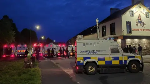 Police under attack in fifth night of unrest BBC A line of police in riot gear. It's night. A number of police land rovers are parked.