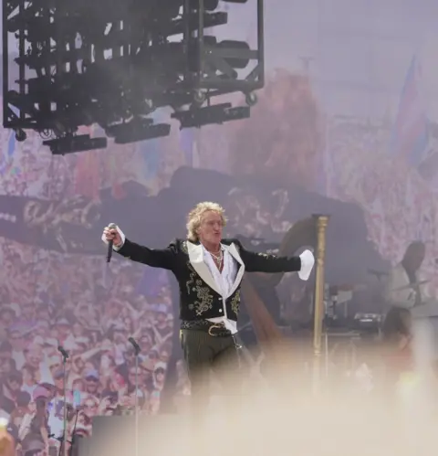 Old school charm from another era Getty Images Rod Stewart on stage at Glastonbury with arms outstretched in front of a big screen, showing a large audience