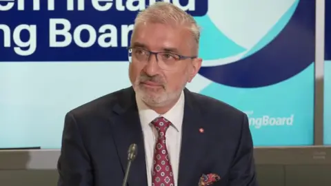 Families hid in attics during 'race motivated' disorder, says chief constable A man is sitting at a table talking to the media through a mic. He's wearing a navy suit and a patterned tie. A pocket square is in his jacket.