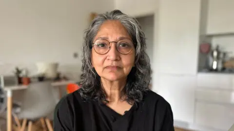 'It was sold as a dream but became a nightmare' Fatima, a woman with shoulder-length greying hair, wearing glasses and a black top