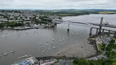 NHS and education named as local priorities BBC A drone shot of Tamar Bridge. The train bridge and car bridge are visible. There are sailing boats on the river Tamar. Saltash is on the left and Plymouth is on the right. There are pastel houses on both sides. The water is a dark grey. The sky is full of clouds.