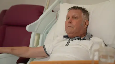 Hospice staff tell BBC what they think about bill BBC Jabez Petherick, who has short grey hair and is wearing a white polo shirt with grey collar while lying on a hospice bed.