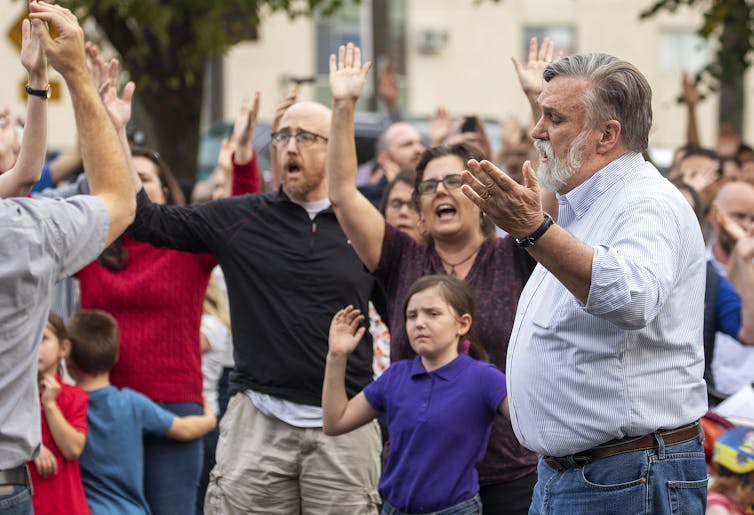 What is CREC? The Christian nationalist group has a vision for America and Defense Secretary Pete Hegseth’s support Several men and women, accompanied by children, appear to be singing, while raising their hands.