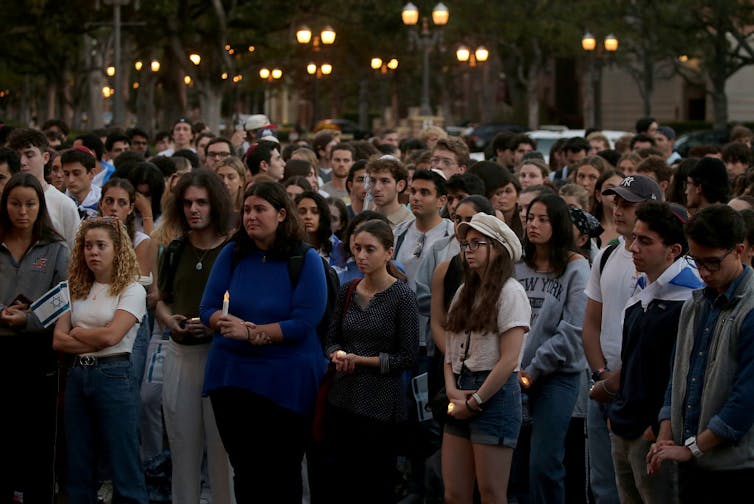 A large group of young people standing outside at dusk, with some holding candles.