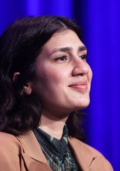 Germany’s young Jewish and Muslim writers are speaking for themselves – exploring immigrant identity beyond stereotypes A close-up photograph of a softly smiling brunette woman in a tan blazer, sitting in front of a blue curtain.