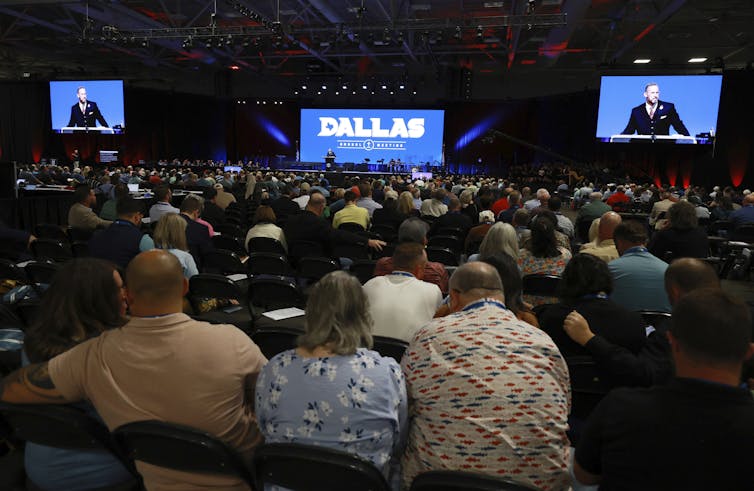 Southern Baptists’ call for the US Supreme Court to overturn its same-sex marriage decision is part of a long history of opposing women’s and LGBTQ+ people’s rights A large audience is seated in a darkened hall, listening to a speaker who appears on two large screens at the front, alongside another screen displaying the words 'Dallas Annual Meeting.'