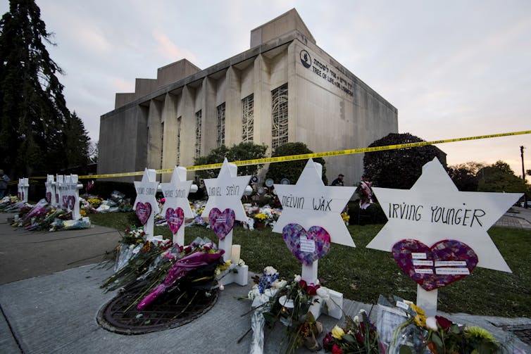 A makeshift memorial outside a building with heart-shaped signs and flowers laid out next to names.