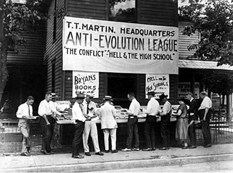 Pop culture helped fan the flames of the Scopes ‘monkey trial’ 100 years ago − and ever since A black and white photo shows men in white shirts gathered around an outdoor book stall.