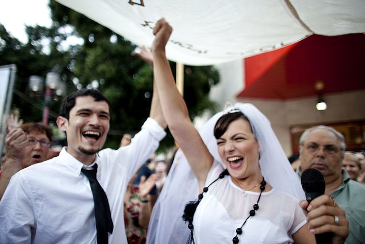 From the marriage contract to breaking the glass under the chuppah, many Jewish couples adapt their weddings to celebrate gender equality A man and woman, both wearing white, smile as they raise their joined hands above their heads.